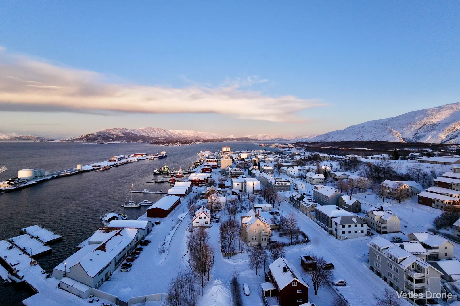 Havna og sentrum i Sandnessjøen i vintersol, med snødekte fjell i bakgrunnen, sett fra drone
