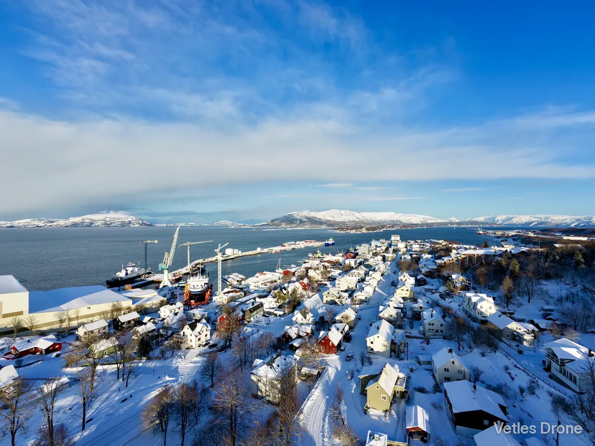 Sandnessjøen med verft, kaier og snødekte hus en solrik vinterdag, med sjøen og fjell i bakgrunnen, sett fra drone