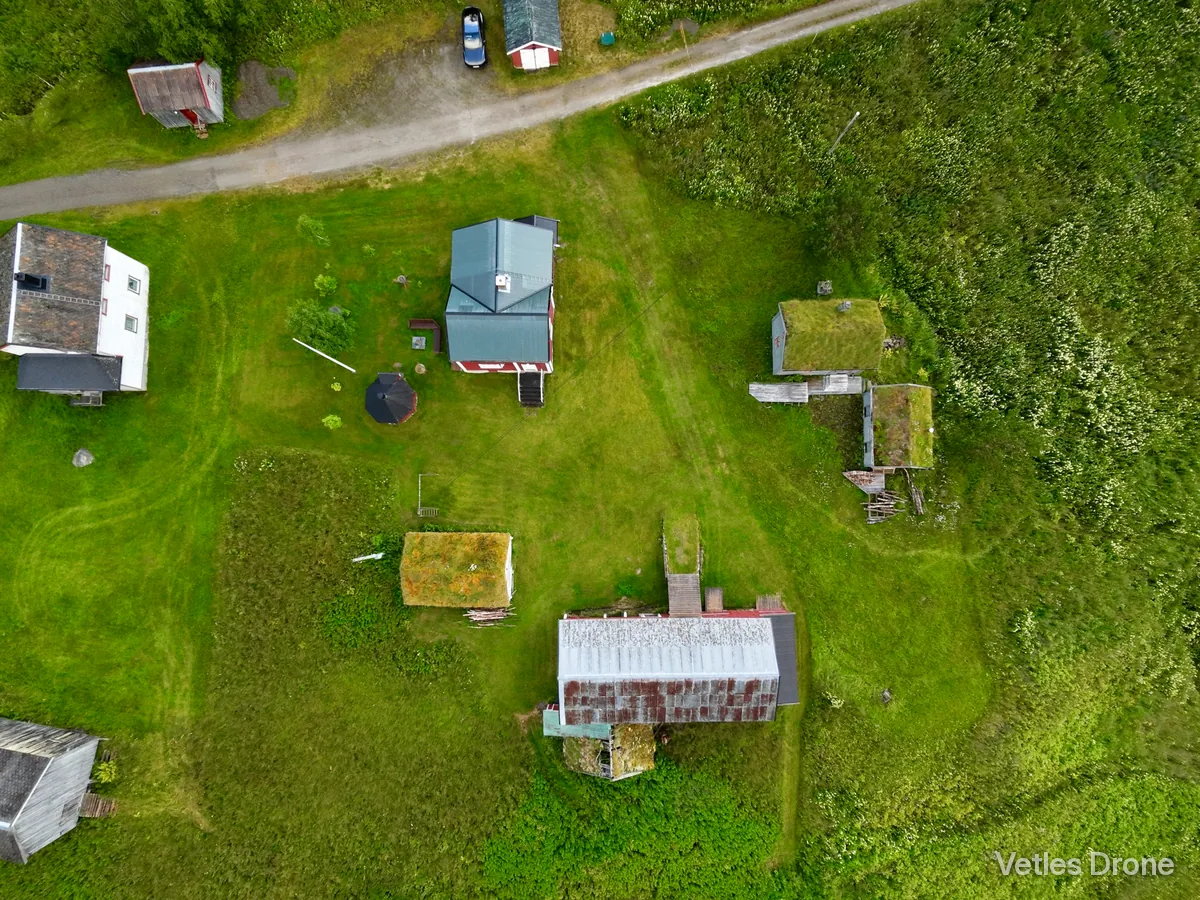 Gårdstun med hus, låve og små uthus med torvtak på en grønn eng, fotografert rett ovenfra