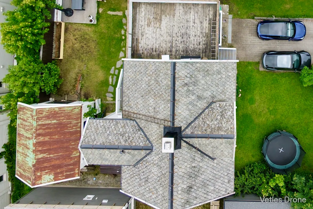 Skifertak med pipe, møner og takrenner, fotografert rett ovenfra med drone